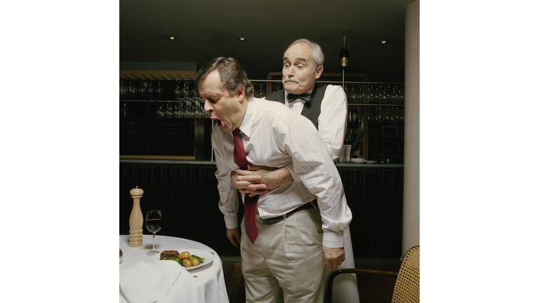 Waiter with arms around choking man's stomach in restaurant