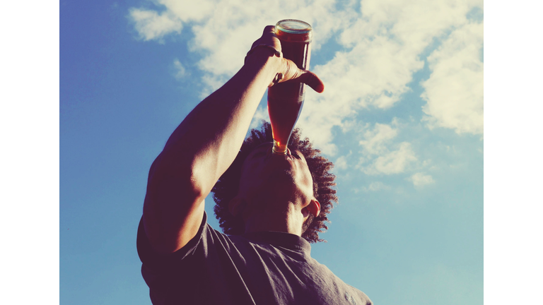 Low Angle View Of Man Drinking Cola Against Sky