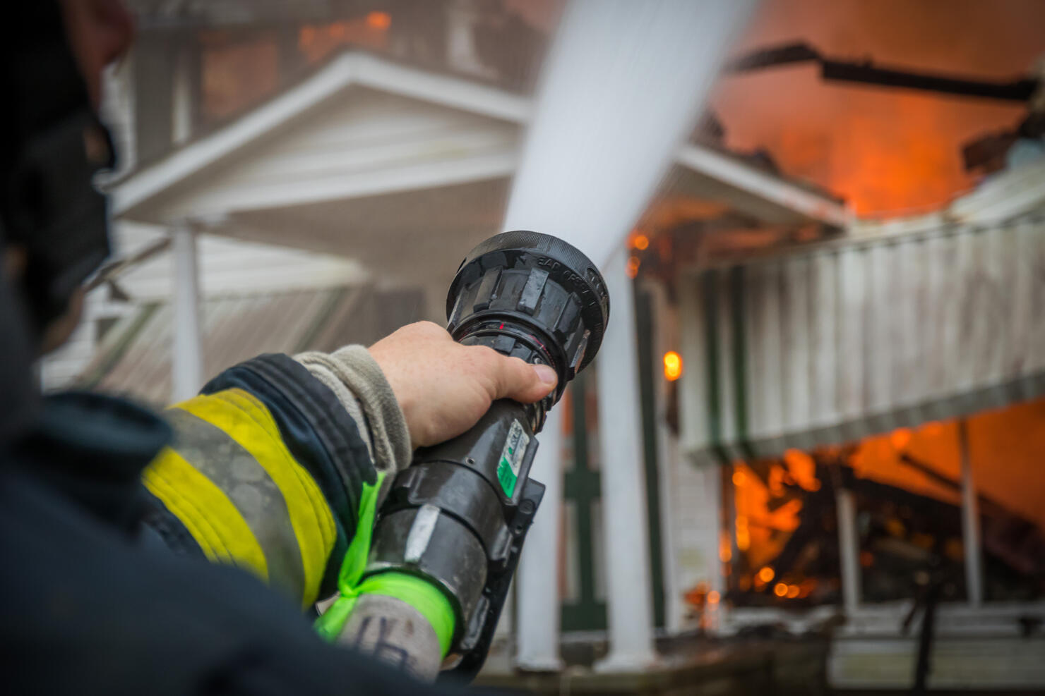 Close-Up Of A Firefighter Spraying Burning House With Hose