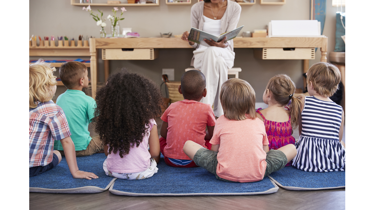 Teacher At Montessori School Reading To Children At Story Time