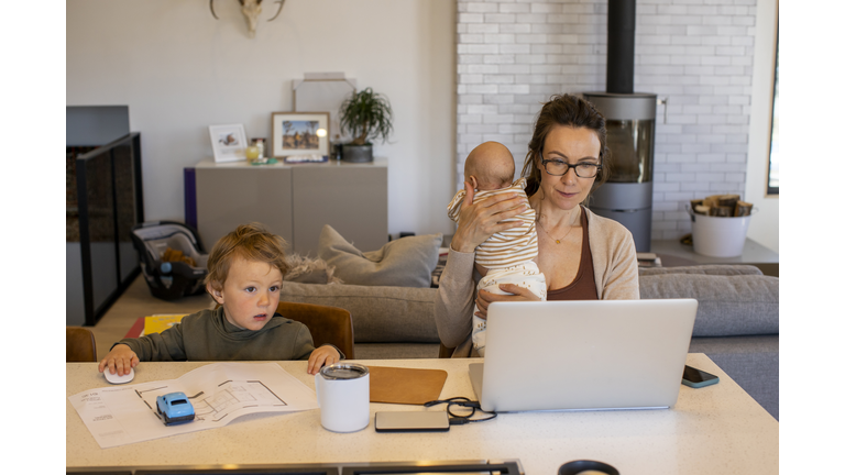 A mom trying to work from home while holding her daughter and watching her son during the COVID-19 home quarantine.
