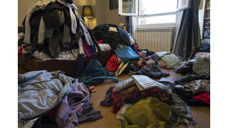 Messy bedroom with clothes and possessions scattered on the floor and bed