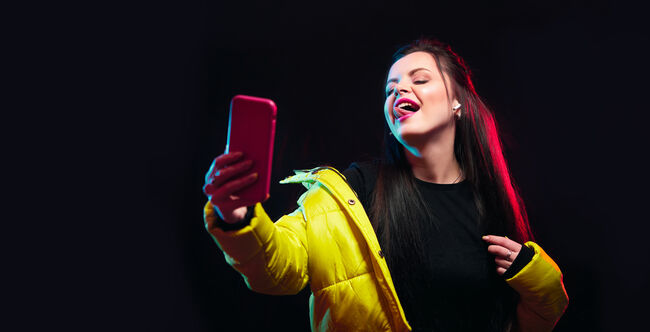 Tik tok advertisement concept.Young girl posing with smart phone in her hands, making selfie on black background.TIK TOK is a popular social network on the internet.Studio shots, copy space for text