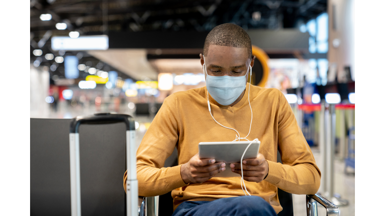 Man wearing a facemask at the airport while watching movies on his tablet at the gate