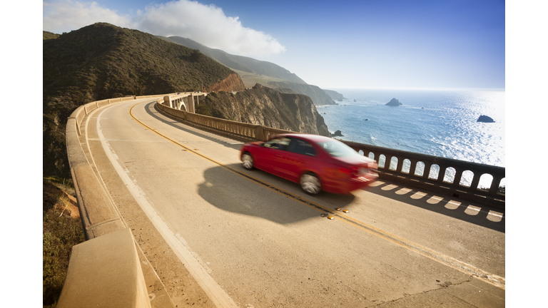 Red car zooms down Bixby Bridge in Big Sur