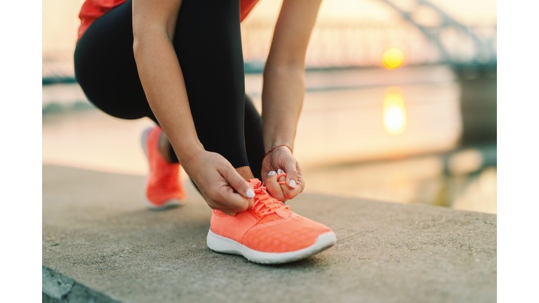 Close up of sporty woman tying shoelace while kneeling outdoor, In background bridge. Fitness outdoors concept.