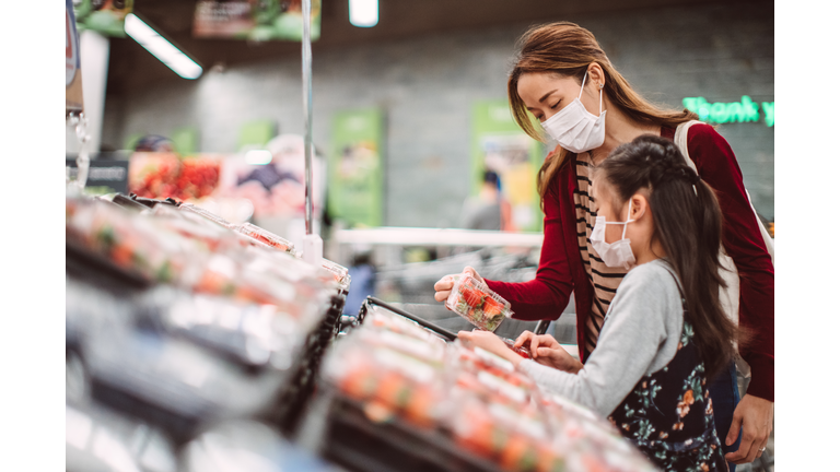 Mom & daughter with surgical masks doing grocery shopping for fresh fruits in supermarket