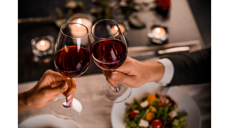 Close up of young couple toasting with glasses of red wine at restaurant