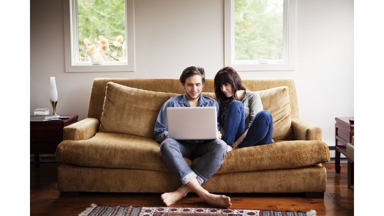 Man using laptop computer while sitting with girlfriend on sofa at home