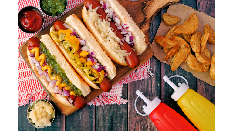 Hot dogs with assorted toppings and potato wedges, overhead scene on wood