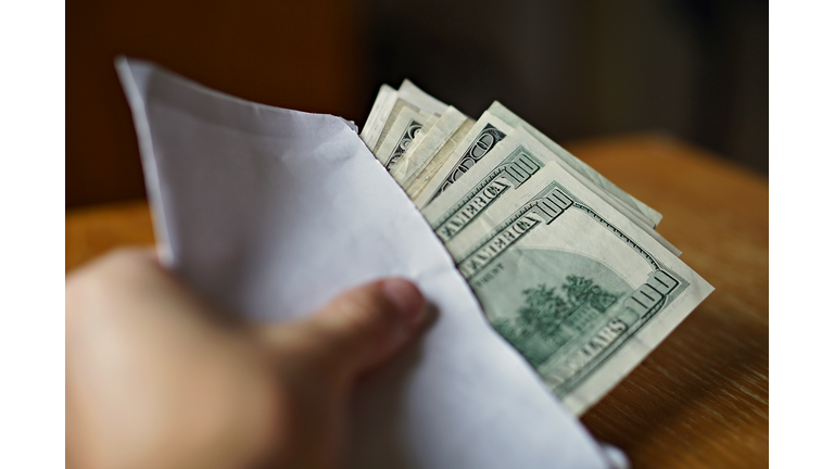 Male hand holding and passing white envelope full of Dollars