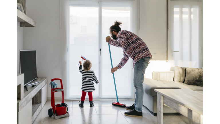 Father and little daughter cleaning the living room together