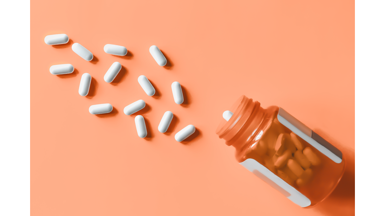 White pills spilling out of prescription bottle onto orange surface