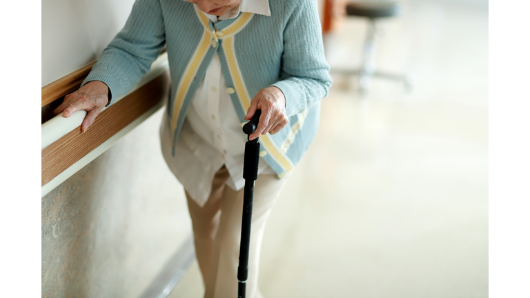 Senior woman walking with walking cane in hospital corridor