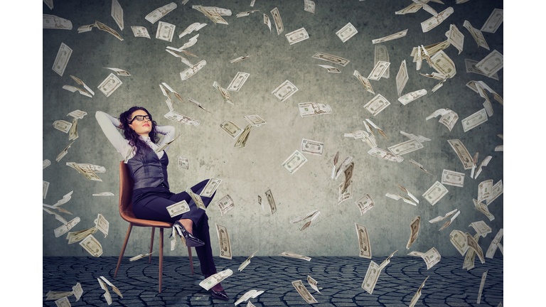 Successful woman sitting under money rain