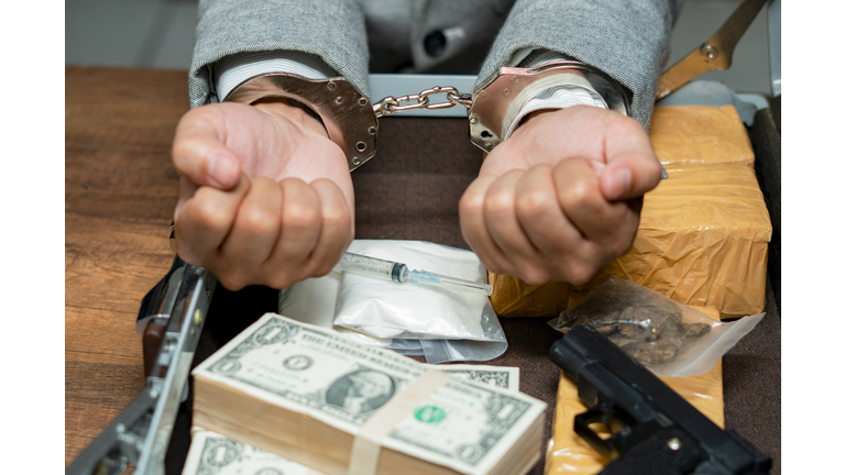 Drugs money and gun on wooden table in concept about danger and threat of the drug,The drug dealer was arrested in handcuffs.