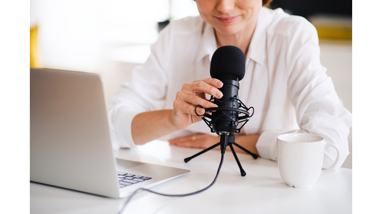 Midsection of woman vlogger or blogger with laptop and microphone, talking.