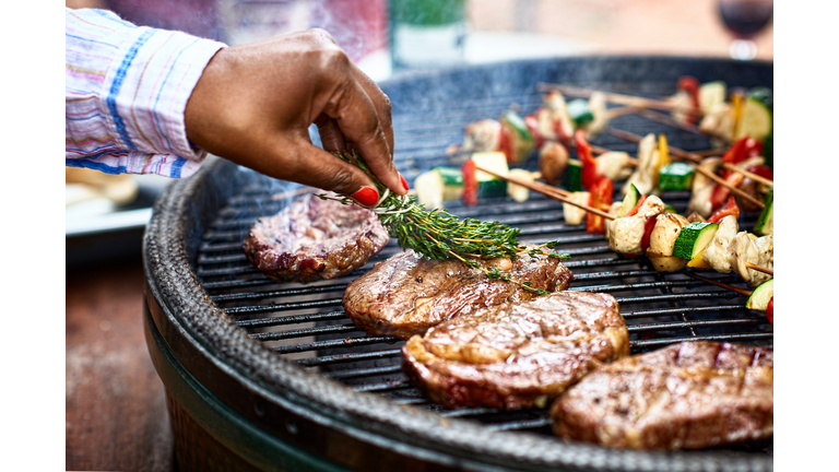 Woman basting meat on barbecue with fresh herbs