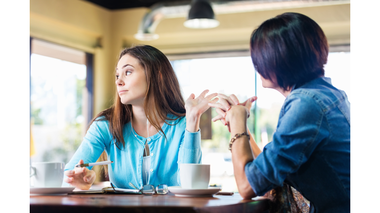 Annoyed teen girl talking to mother in coffee shop