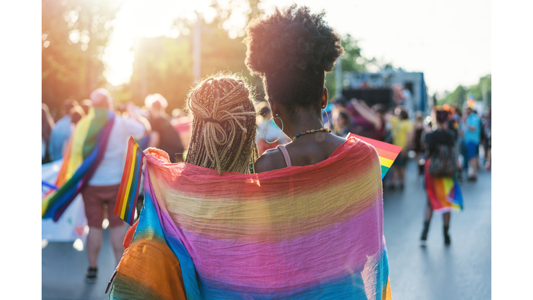 Young female couple hugging with rainbow scarf at the pride event