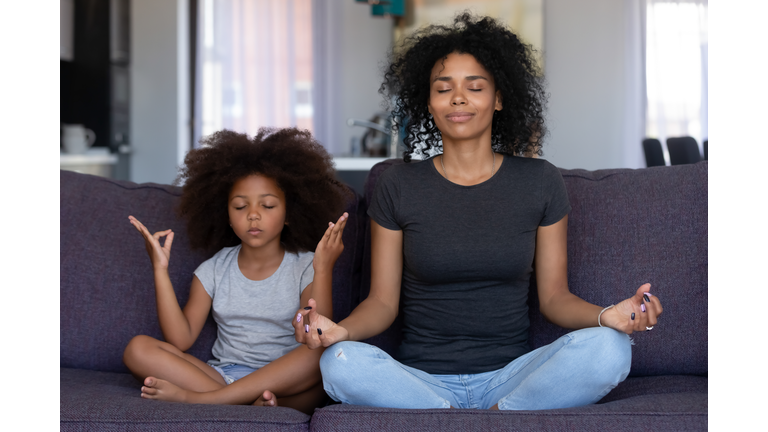 Mindful african mom with funny kid daughter doing yoga together