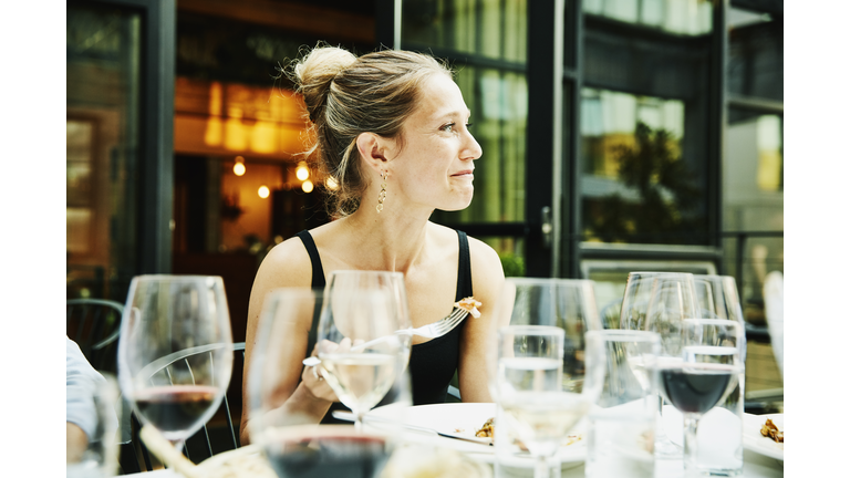 Smiling woman sharing dinner with friends on restaurant patio on summer evening