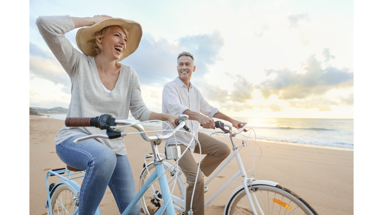 Mature couple cycling on the beach at sunset or sunrise.