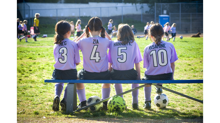 four girls [8] on the bench at soccer game