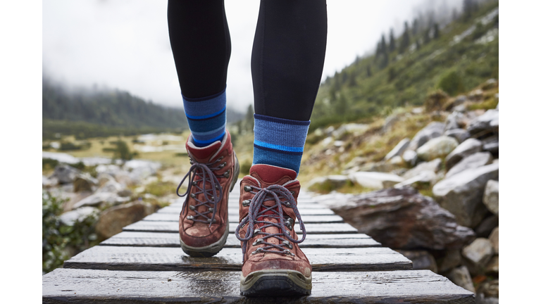 Female hiker hiking across wooden footbridge, cropped view of legs and hiking boots