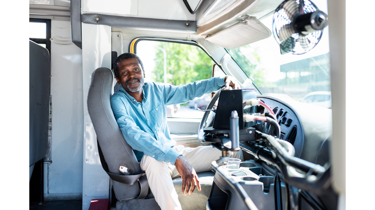 smiling mature african american bus driver looking at camera while sitting inside bus