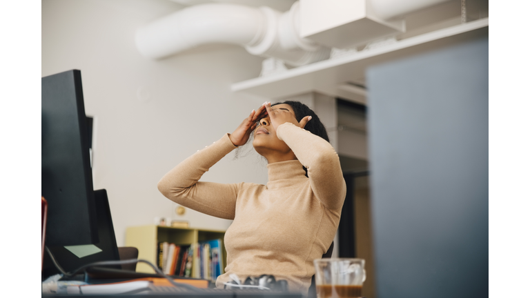 Frustrated female computer programmer with head in hands sitting in creative office