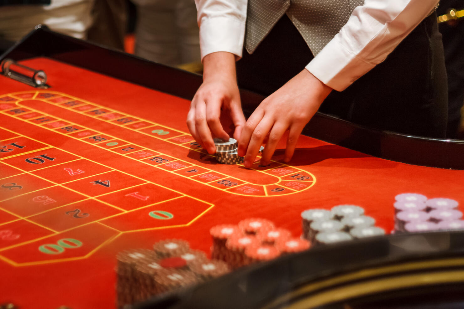 Midsection Of Casino Worker Holding Gambling Chips On Table