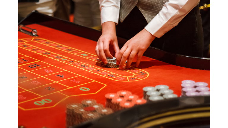 Midsection Of Casino Worker Holding Gambling Chips On Table