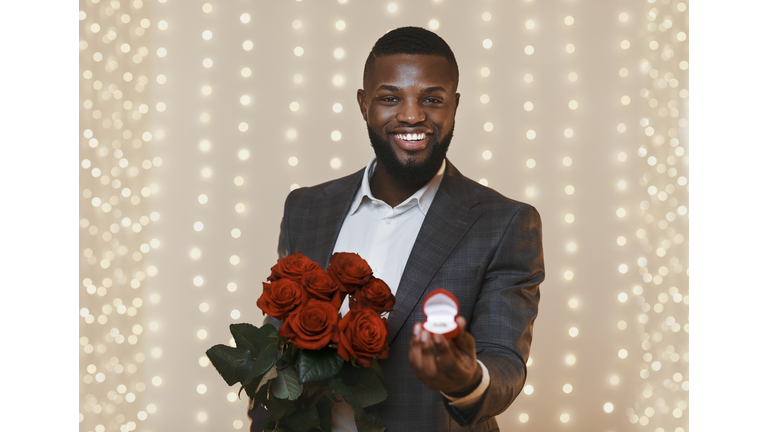 Happy black guy holding red roses and wedding ring