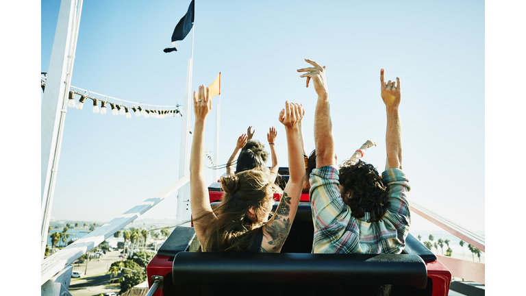 Rear view of couple with arms raised about to begin descent on roller coaster in amusement park