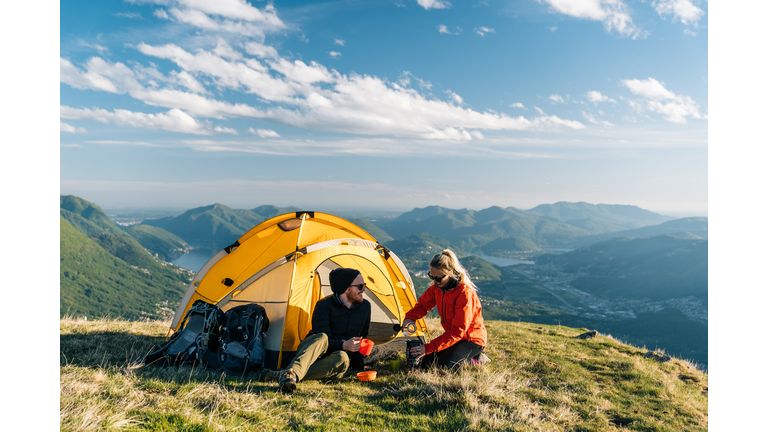 Couple camping on mountain top, prepare food and beverages next to tent