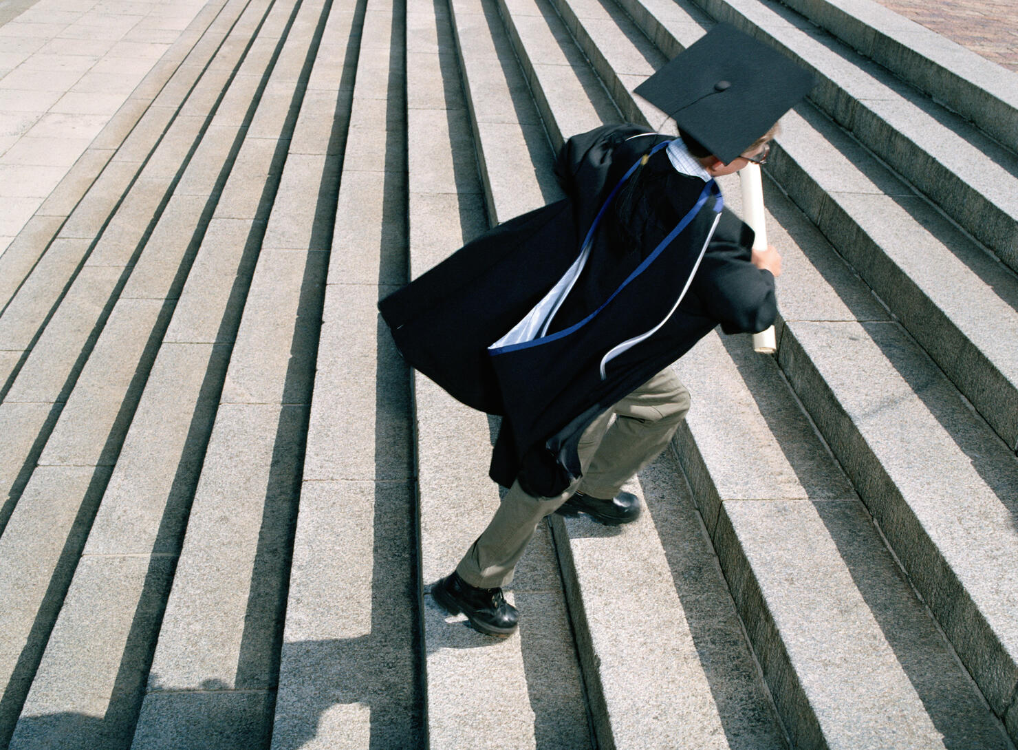 Boy (7-9) wearing graduation cap and gown running up steps