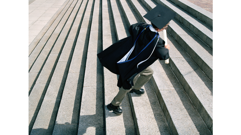 Boy (7-9) wearing graduation cap and gown running up steps