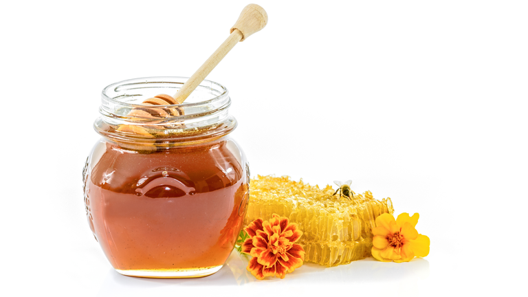 Close-Up Of Honey In Jar And Flowers Against White Background