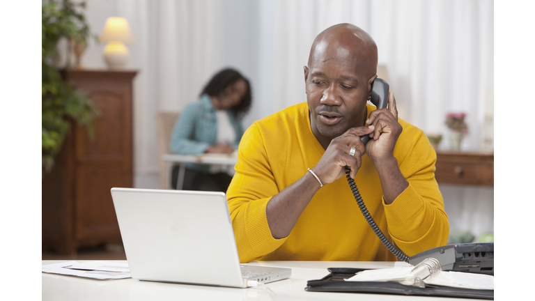 African American man using laptop and talking on telephone