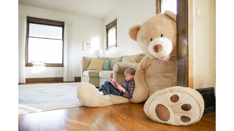 Side view of boy playing game while sitting on large teddy bear at home