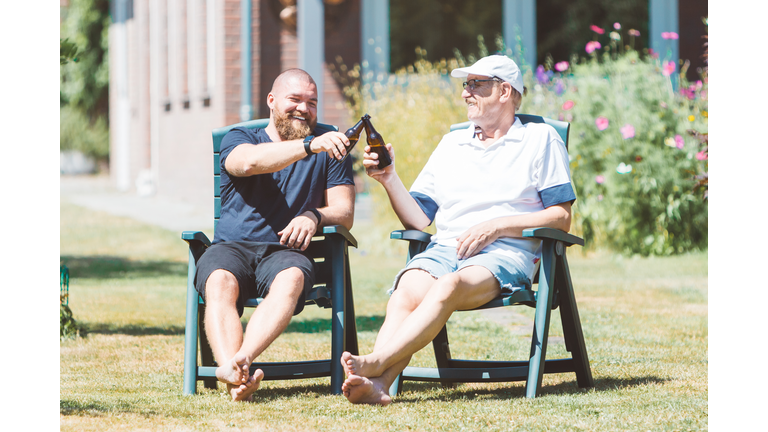Two smiling men (young and old) drinking beer in the summer garden - best friends (father and son) toasting and laughing together - family and Father's Day celebration concept