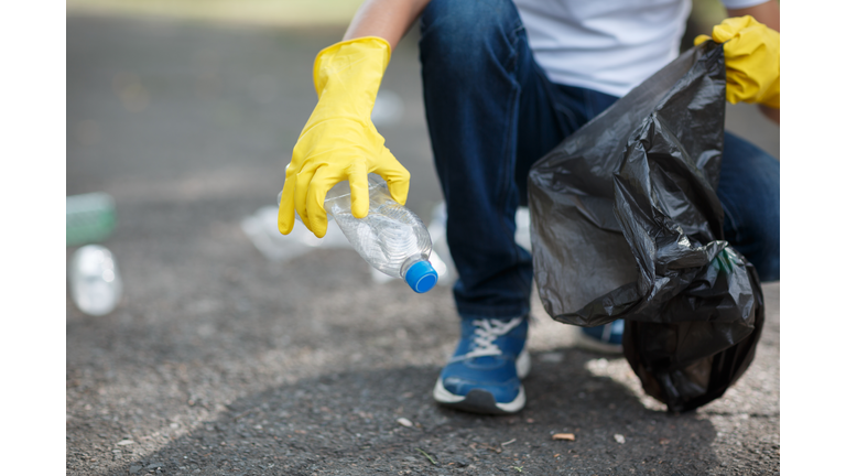 Male hands in yellow rubber gloves putting household waste into small and black bin bag outside.