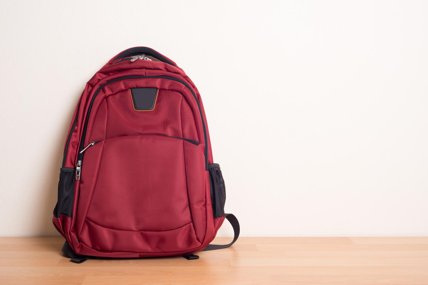Red Backpack On Hardwood Floor Against Wall