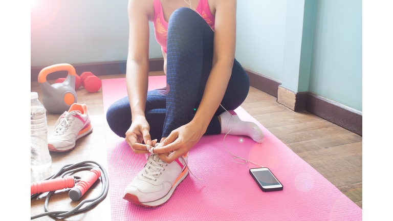 Low Section Of Woman Tying Shoelace While Sitting On Exercise Mat At Home