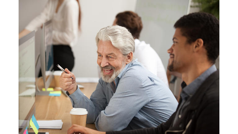 Smiling senior employee discussing email with african colleague at workplace