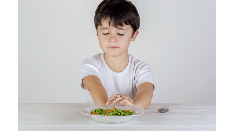 Unhappy Caucasian boy eating vegetables