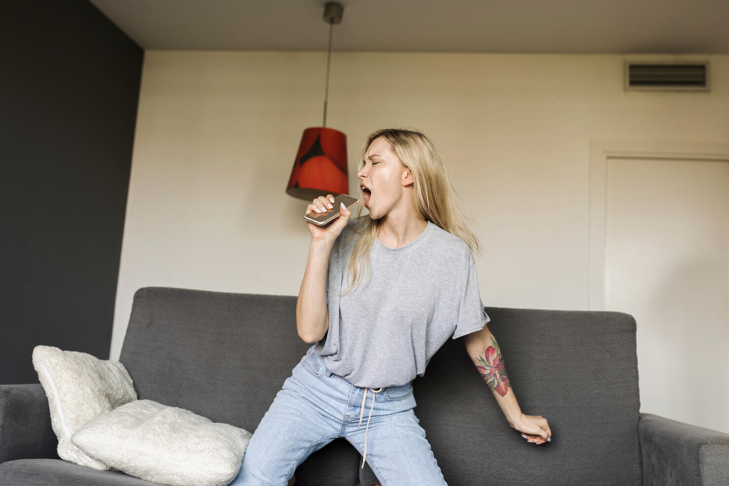 Exuberant young woman on couch with cell phone pretending to sing
