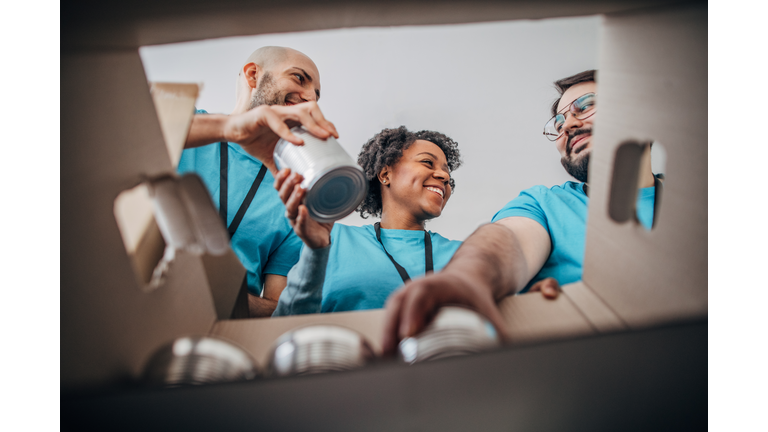 Diverse volunteers packing donation boxes with canned food in food bank