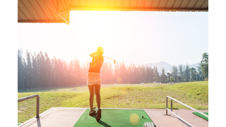 Young woman practices her golf swing on driving range, view from behind,Young girls practicing driving range.